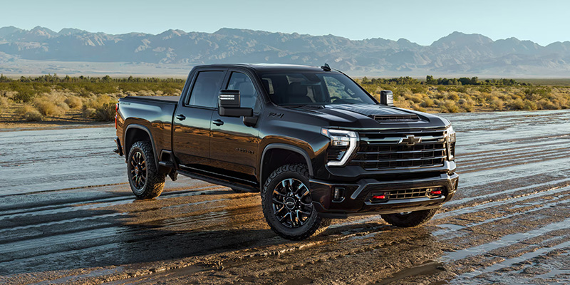 A black 2026 Chevrolet Silverado HD truck parked in a desert landscape, showcasing its rugged design and powerful stance.