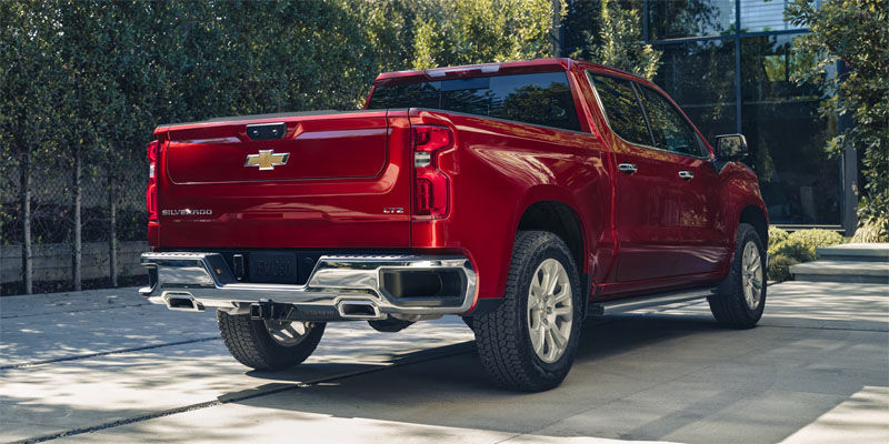 Rear view of a red Chevrolet Silverado pickup truck parked on a concrete driveway with trees and landscaping in the background