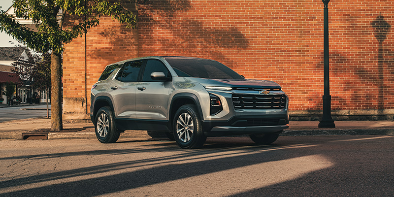 Front three-quarter view of a gray Chevrolet SUV parked on a city street in front of a brick wall, showcasing its bold grille and modern exterior styling.