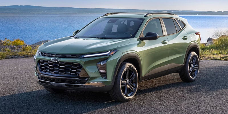 Green Chevrolet SUV parked near a scenic waterfront with a mountain backdrop.