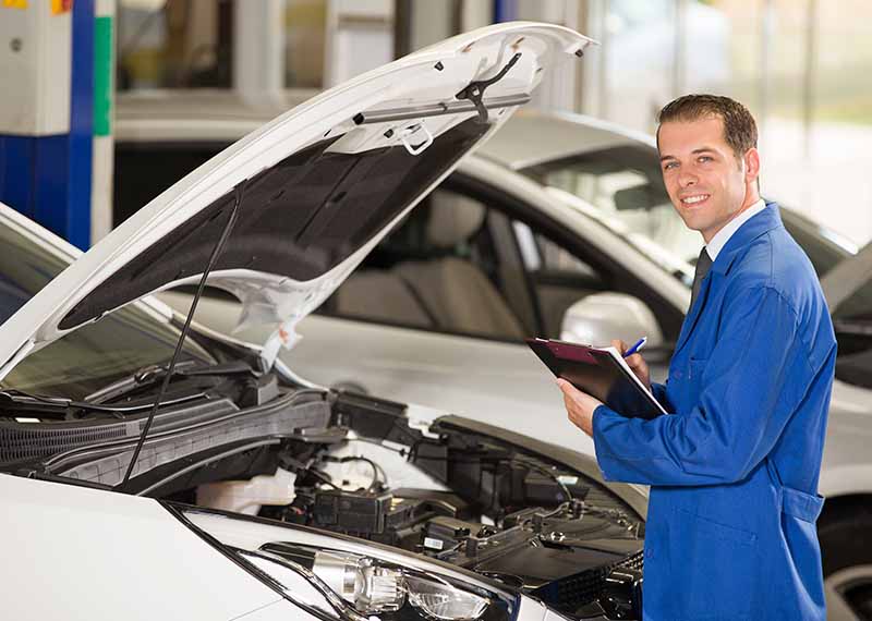 Automotive technician inspecting a vehicle engine with the hood open in a service center.